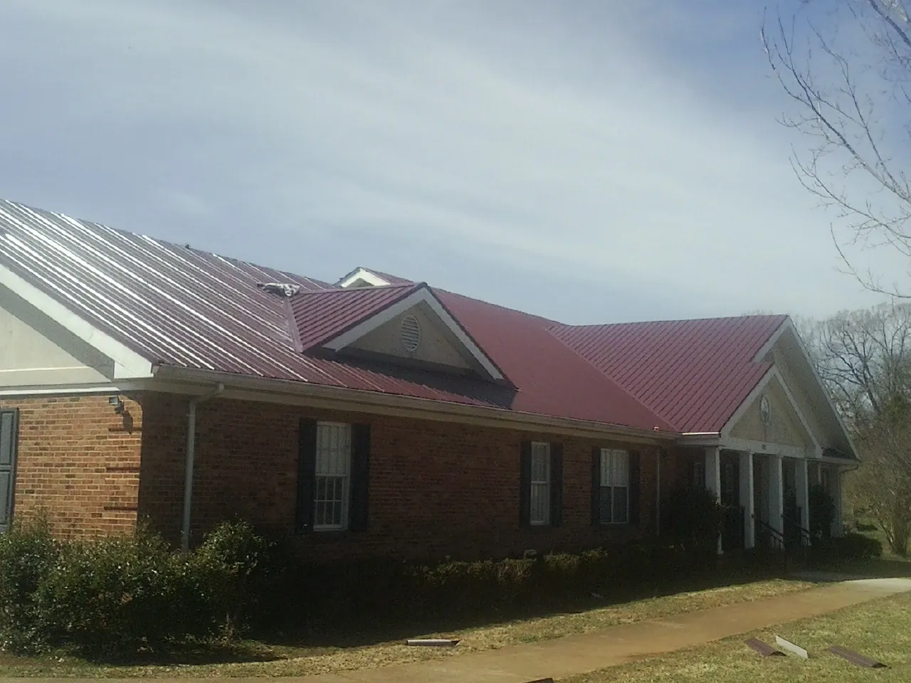 Red metal roof with gabled entries on a long brick building, from a Hail Damage Roof Repair job in Wheeling