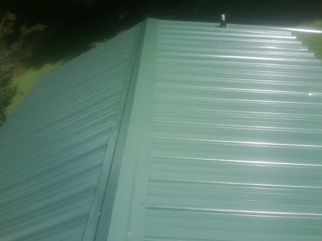 New green metal panels meeting at the ridge of a roof — Flat Roof Repair work by our crew in Wheeling