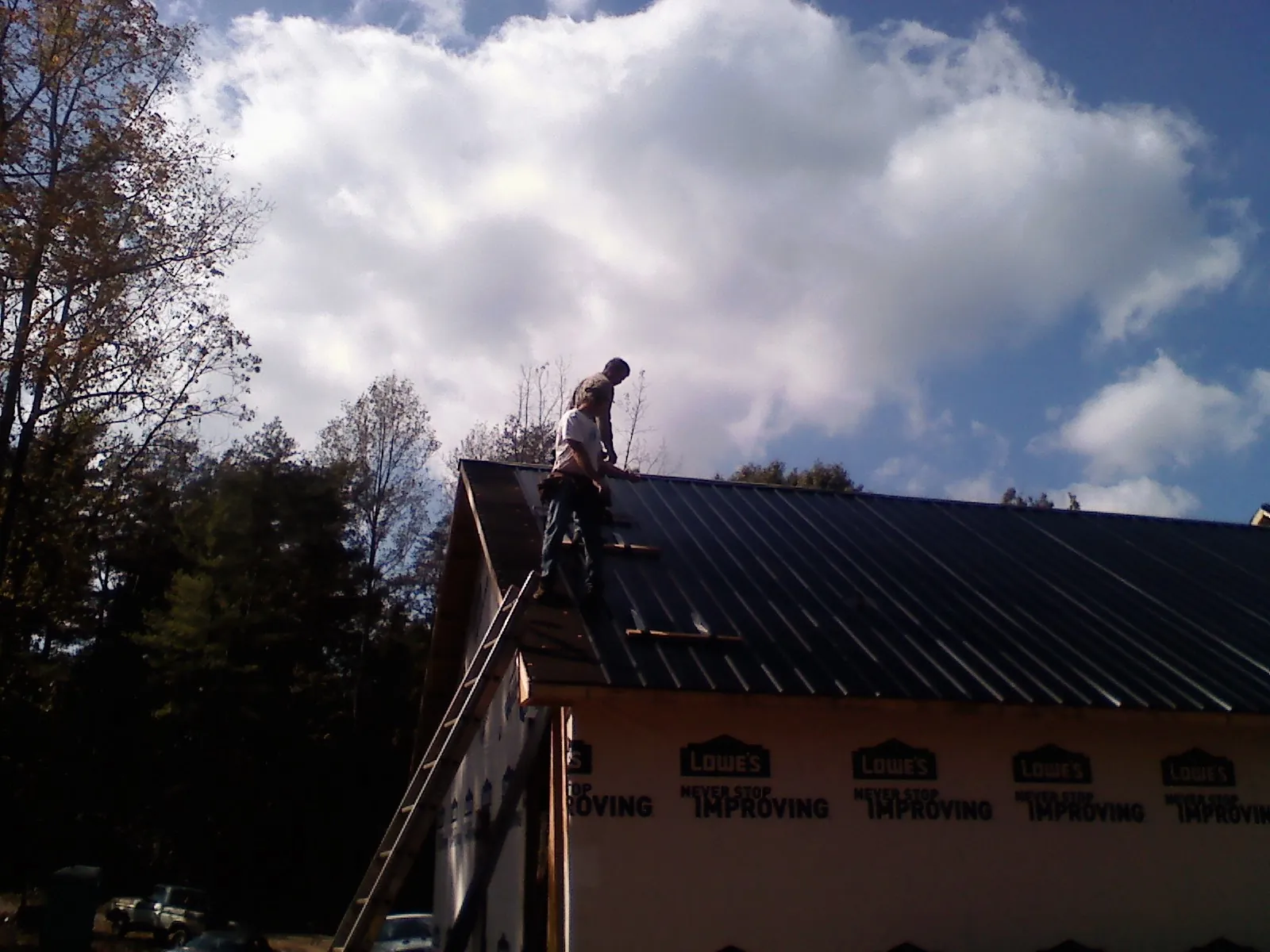 Roofer fastening dark metal panels high against a cloudy sky, from a Roof Inspection job in Wheeling